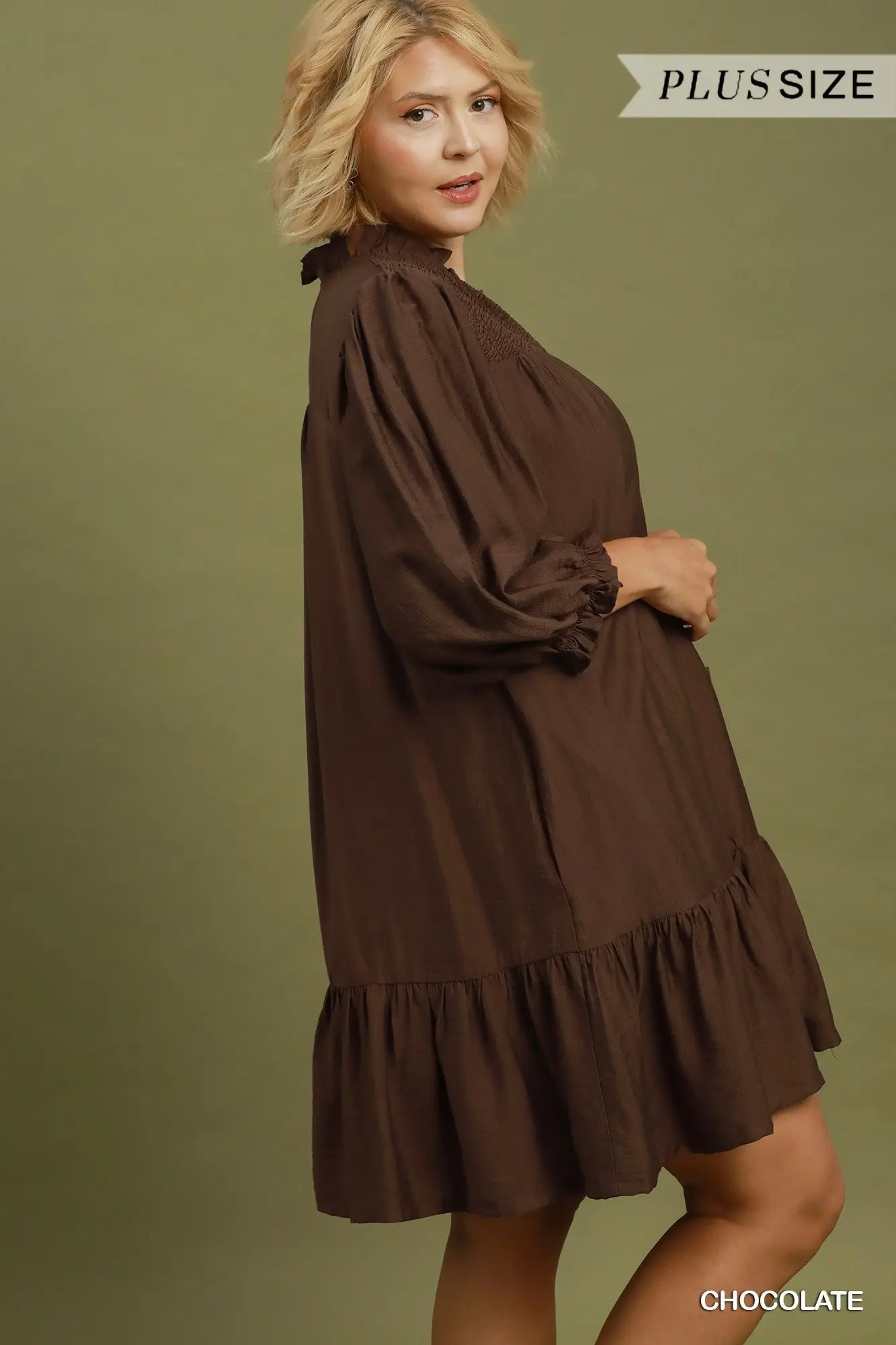 Loose-fitting brown long-sleeve mini dress with smocked details, ruffled tiers, and flowy silhouette. Available in sizes XS-XL.