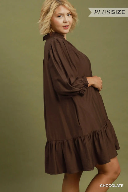 Loose-fitting brown long-sleeve mini dress with smocked details, ruffled tiers, and flowy silhouette. Available in sizes XS-XL.