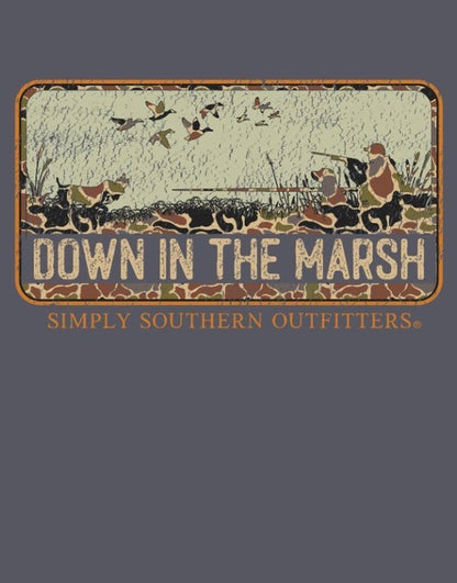 The Down In The Marsh Graphic Tee features a rustic “DOWN IN THE MARSH” sign with silhouettes of hunters, dogs, and flying ducks; bold orange “SIMPLY SOUTHERN OUTFITTERS” lettering sits below the scene on a dark background. Available in sizes S–XXL.