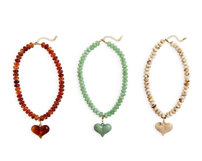 Chunky beaded necklace with a heart pendant, available in amber, green, or beige beads. Features gold clasp and chain extender. Sizes: S, M, L.