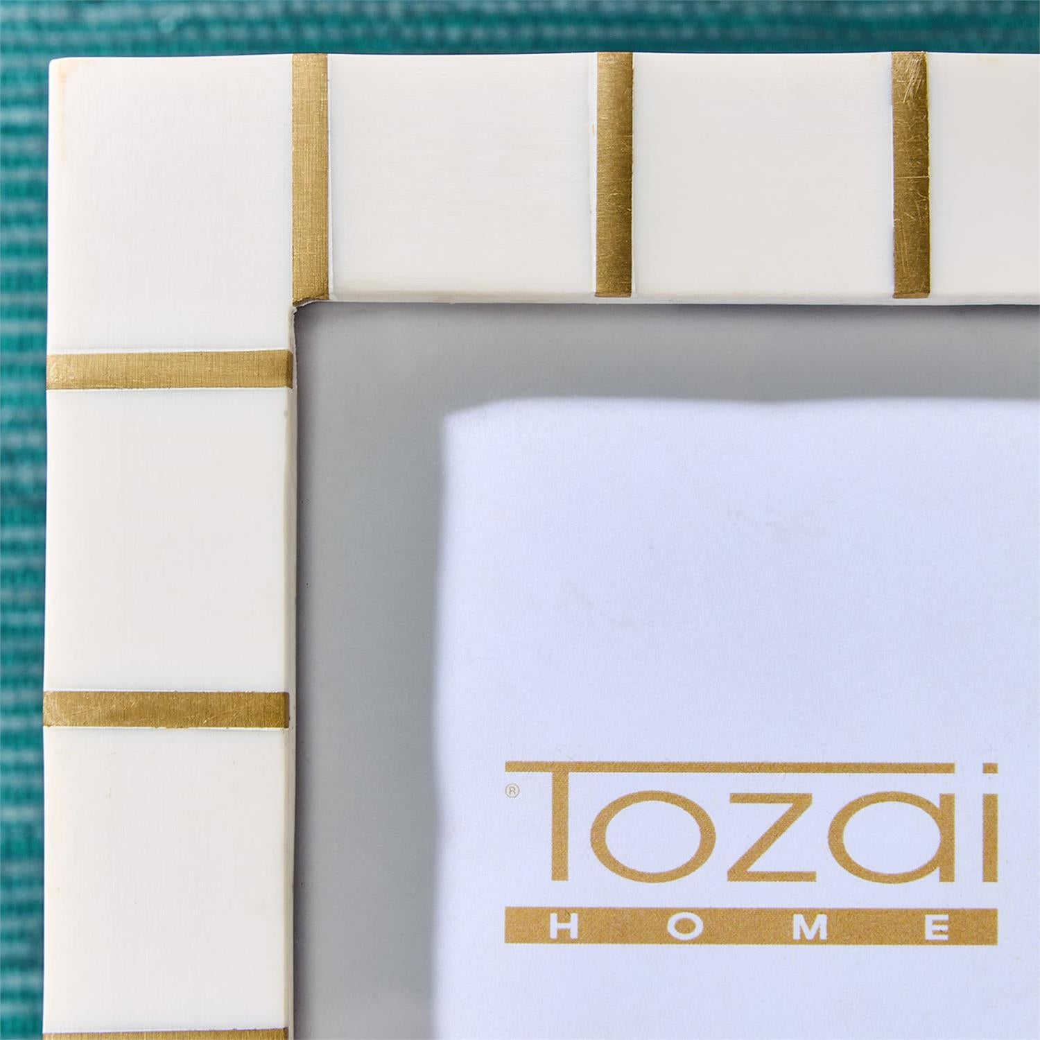 Brass Lines Photo Frame in white resin with gold vertical stripes, displaying a “Tozai HOME” insert in gold text. Available sizes: 4x6, 5x7.