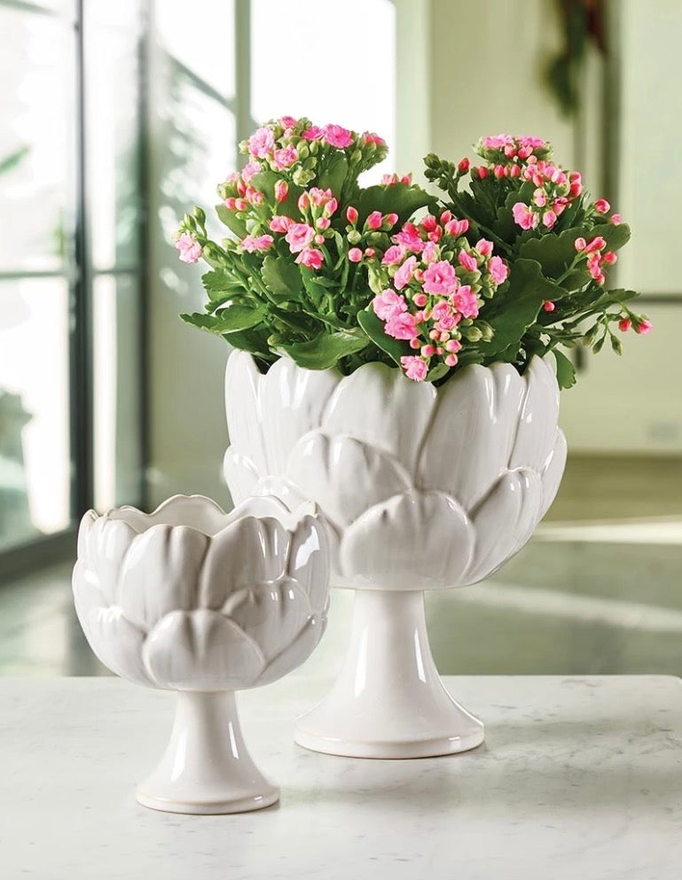 White ceramic vases shaped like flower petals, available in small and medium sizes, each holding a green plant with small pink flowers.