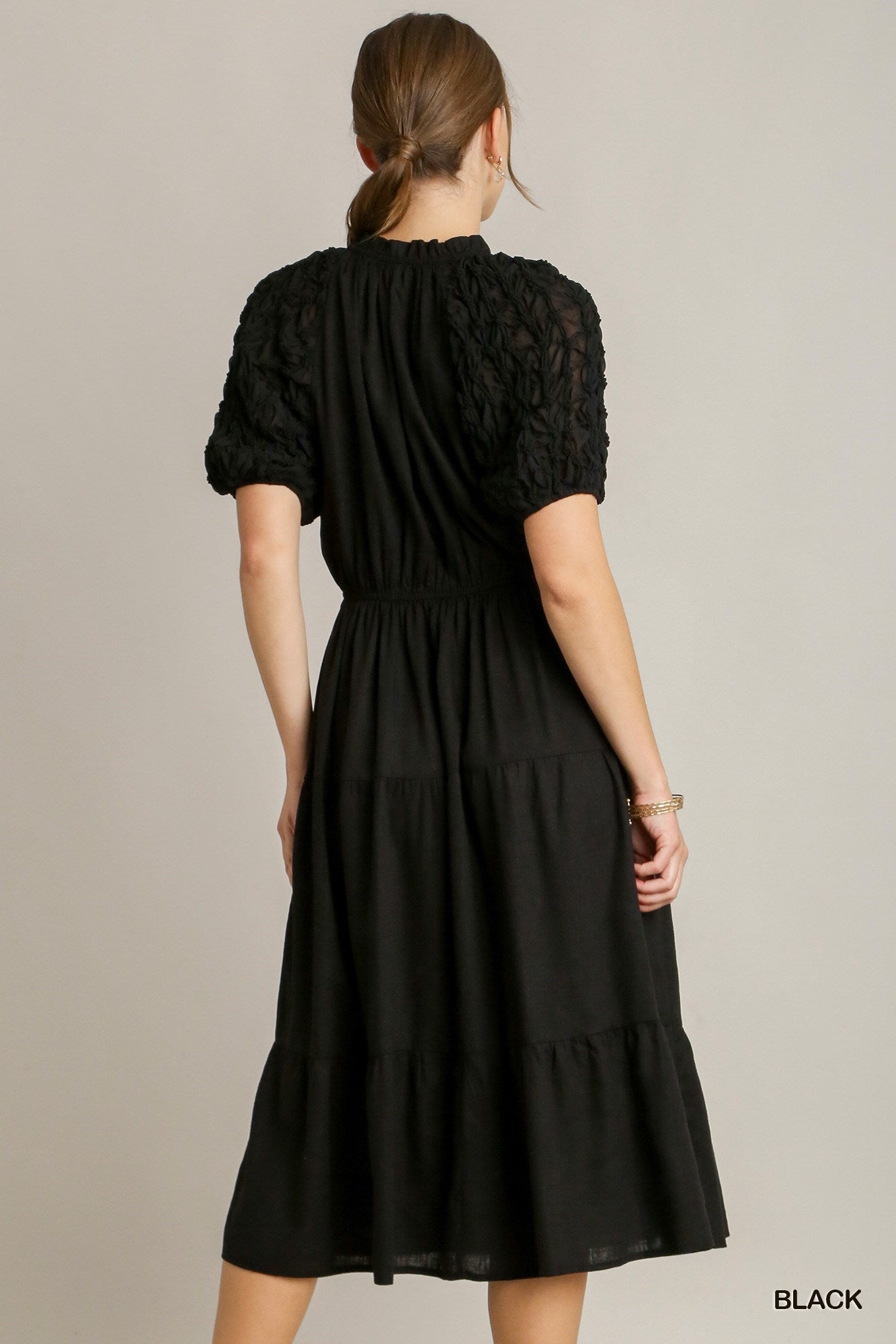 This product is a black Ruffle Tiered Midi Dress. Key features include a Front Tassel Drawstring and Textured Sleeves. Sizes available range from XS to XL.