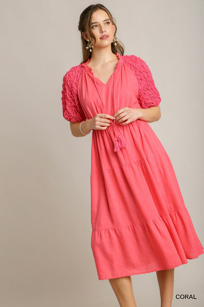 Coral Linen Midi Dress with textured puffy sleeves, V-neck, tassel tie at waist. Sizes: XS, S, M, L, XL.