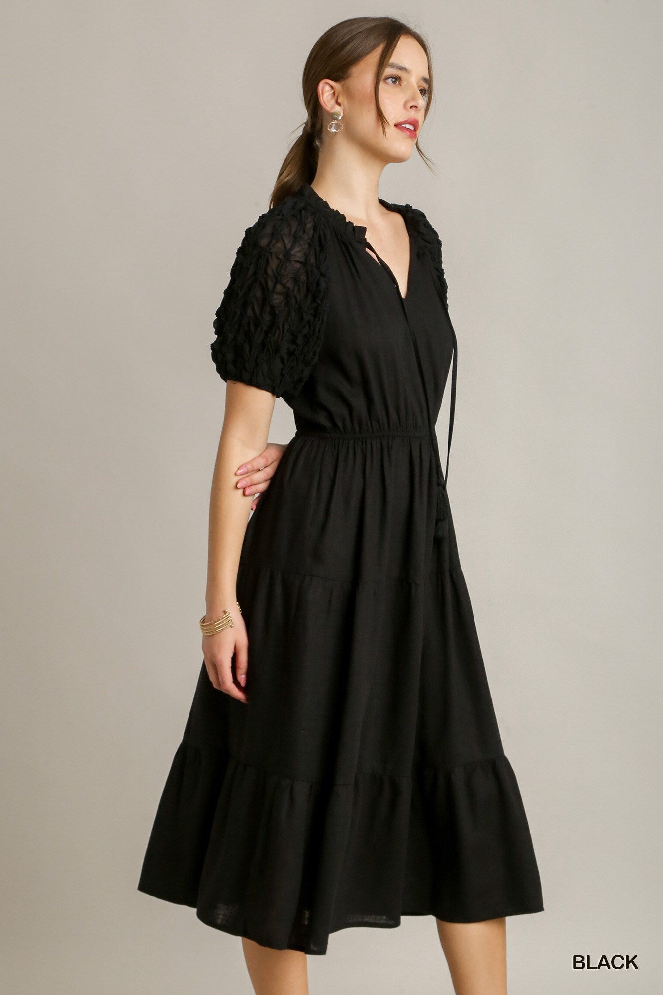 This Ruffle Tiered Midi Dress comes in an elegant black color. Features include a front tassel drawstring and unique textured sleeves. Available sizes for this product vary.