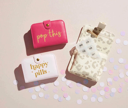 Two compact pill cases, pink "pop this" and white "happy pills." Sizes available: small. Weekly organizer not included.