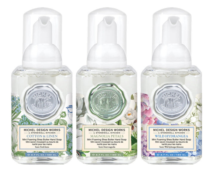 Three bottles from the Mini Foaming Hand Soap Set by Michel Design Works. Each showcases distinct botanical designs and contains fragrances like Cotton &amp; Linen, Magnolia Petals, and Wild Hydrangea. Available in a mini set size.