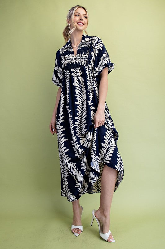Navy blue midi dress with white leaf print, short puff sleeves, and smocked bodice. Available in multiple sizes.