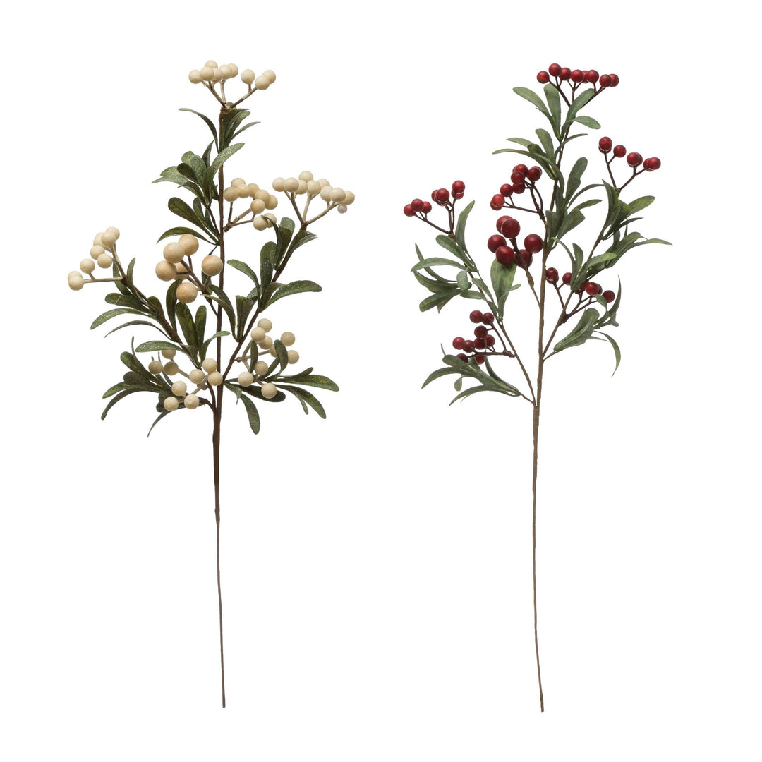 Two faux berry and leaf branch stems, one with green foliage and white berries and one with green foliage and red berries.