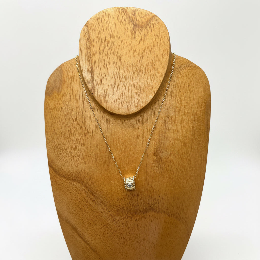 The Ezra Gold Pendant Necklace features a small cylindrical pendant with subtle crystal accents. Available in 16, 18, and 20 inch lengths.