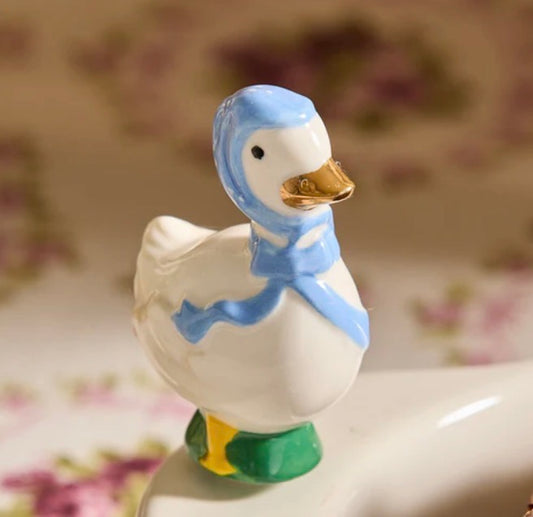 Ceramic goose figurine with blue bonnet, blue ribbon, yellow feet, and green base. Available sizes: small, medium, large.