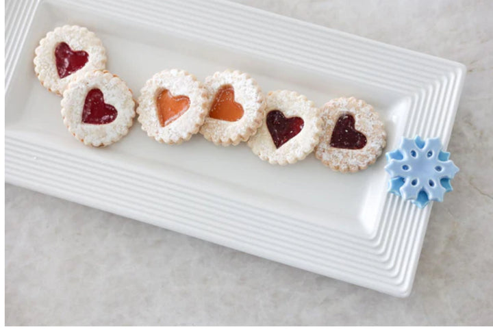 The Bread Tray Stripes: Rectangular white plate with a blue snowflake decoration, holding six cookies. Each cookie has a heart-shaped jam center (three red, three orange) and is dusted with powdered sugar. Available in sizes: Small, Medium, Large.