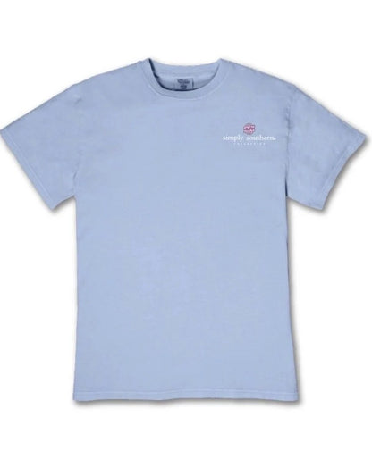The Walking By Faith Tripping Constantly T-Shirt is light blue with short sleeves, a small “Simply Southern” logo, and a pink turtle graphic on the upper left chest. Available in multiple sizes.