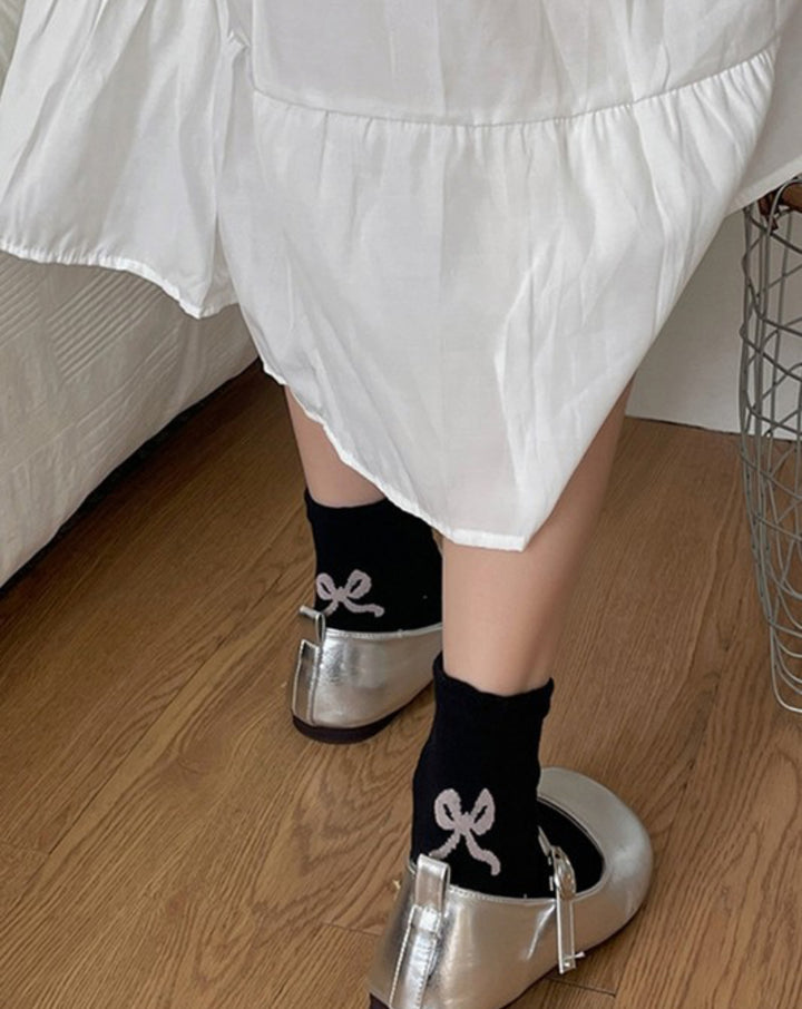 The product is a pair of black, mid-calf socks featuring contrasting bow designs. The socks are available in one size that fits all.