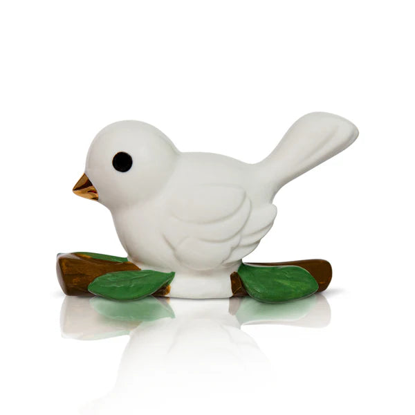 Small white ceramic dove with yellow beak and black eye on brown branch with green leaves. Available in mini size.