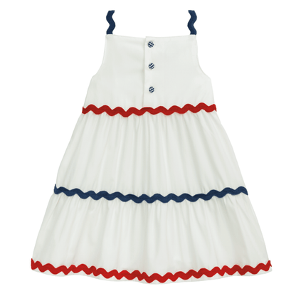 White sleeveless dress with blue straps, chest buttons, and red and blue zigzag trim. Available in sizes 2T-6.