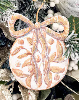 Flat round gold ornament with painted leaves and a decorative bow top.
