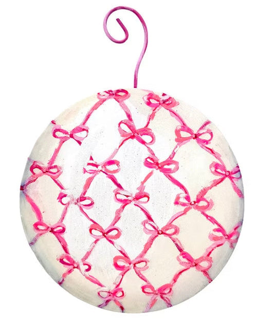 Round pink ball ornament with a white lattice bow pattern and pink hanging hook.