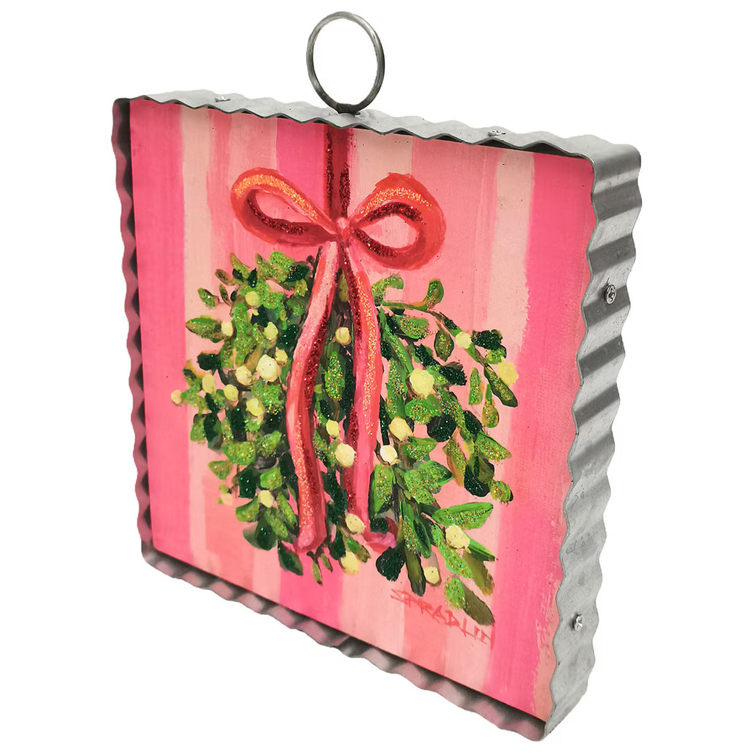 Mini Gallery Art Mistletoe square wall hanging featuring mistletoe art with a red glittery bow, pink striped background, and corrugated metal frame with a hanging loop.