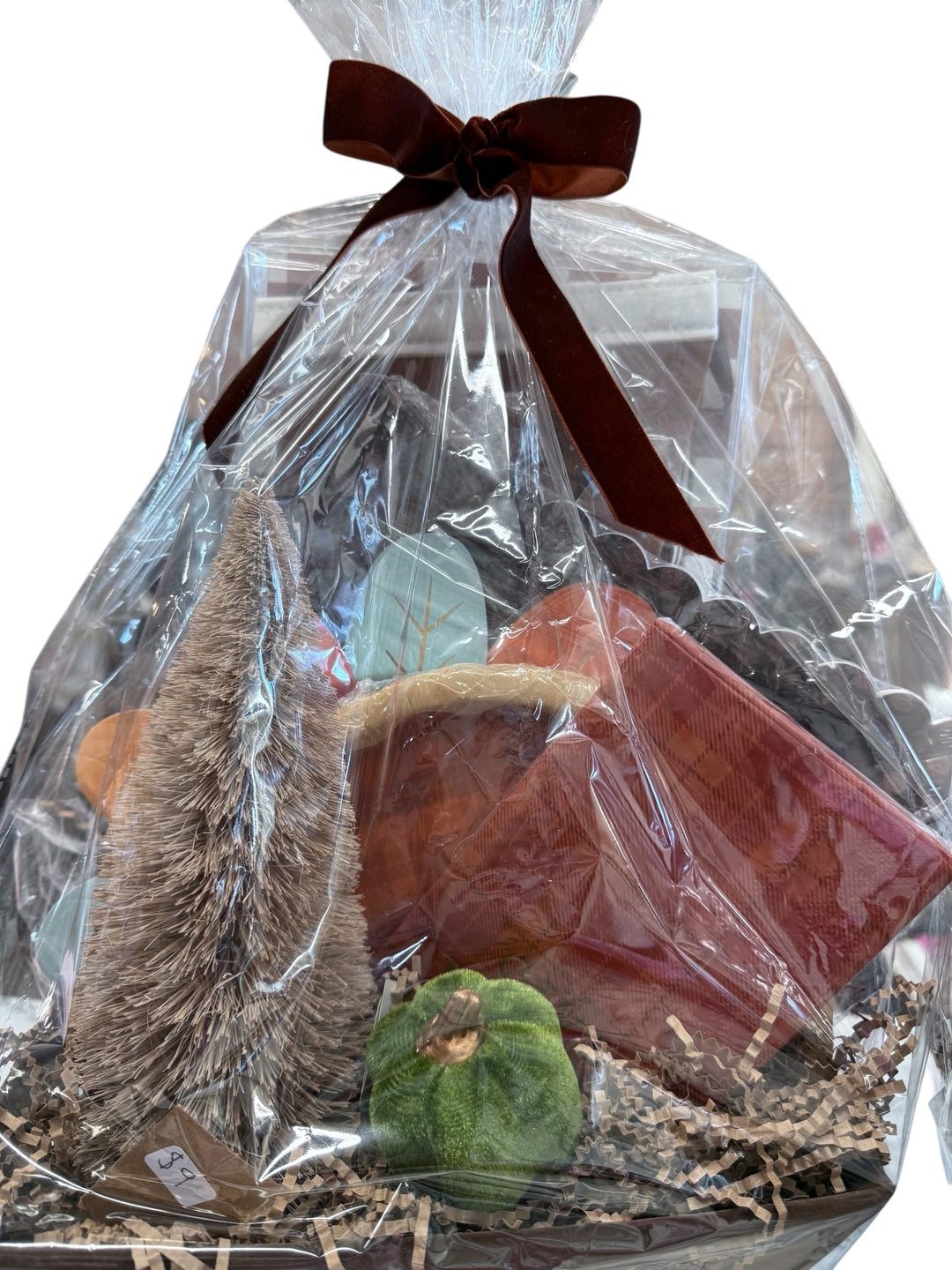 Thanksgiving Basket wrapped in clear plastic with a velvet bow; includes mini tree, green pumpkin, brown wallet, and shredded paper. Sizes available upon request.
