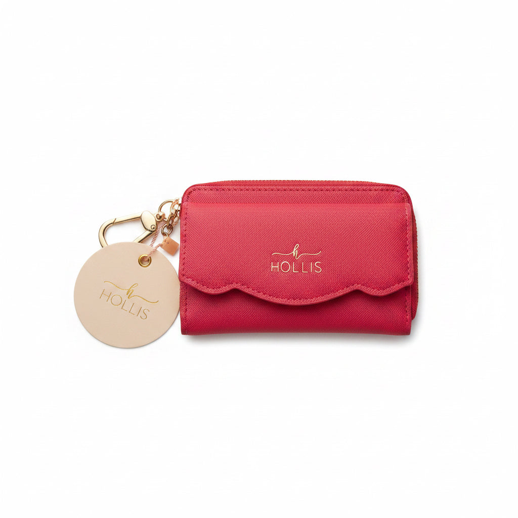 Petite pink cardholder with scalloped edging, gold zipper, attached gold keychain, and embossed “HOLLIS” with bird logo on the front. Features a scalloped front pocket. Size: available in one size.