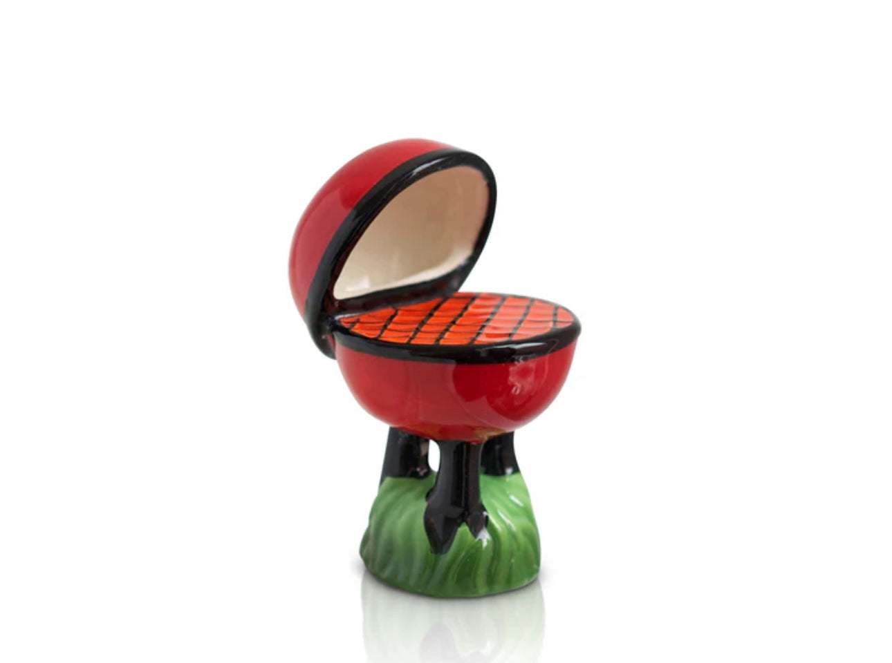 Miniature ceramic barbecue grill from the Nora Fleming Minis collection. Features a red lid, orange grill surface, and green grass stand. Available in standard size only.