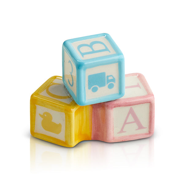 Three pastel Nora Fleming Minis—blue, yellow, and pink—featuring duck, truck, and “B”/“A”, available in standard mini size.