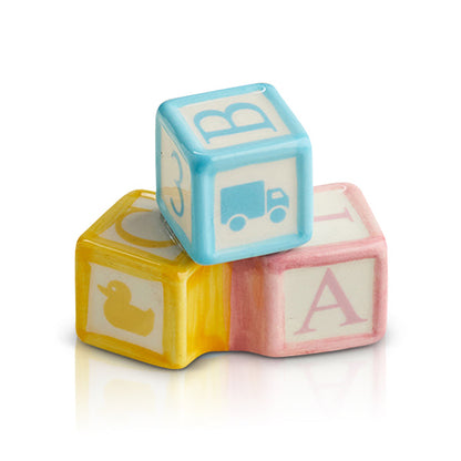 Three pastel Nora Fleming Minis—blue, yellow, and pink—featuring duck, truck, and “B”/“A”, available in standard mini size.