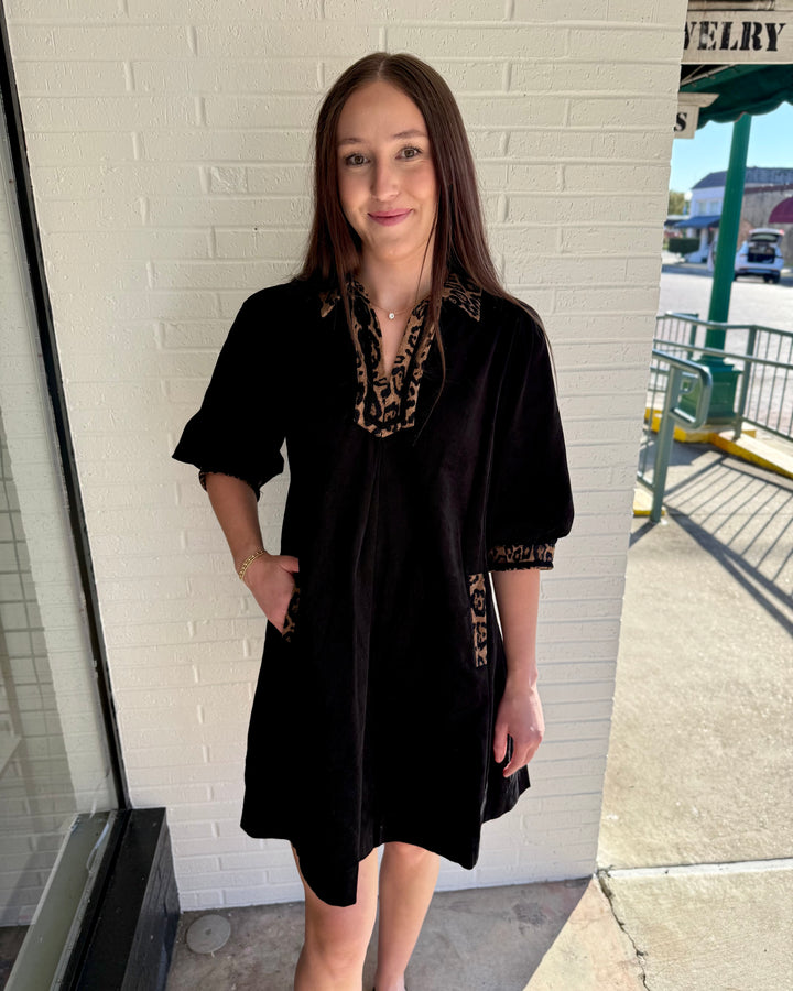 Black V-neck dress with leopard-print trim on collar, sleeves, and side pockets. Available in all sizes.
