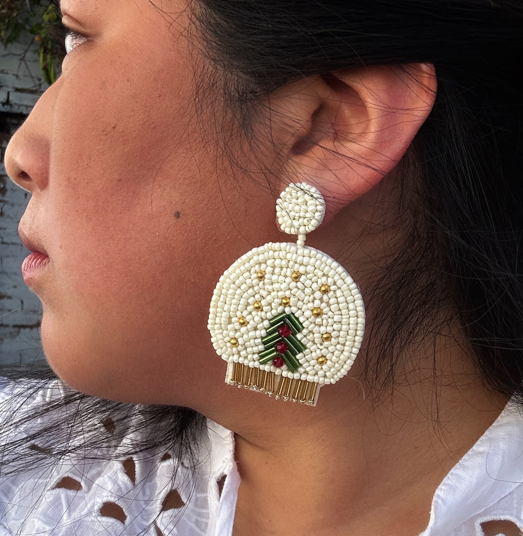 Beaded round Christmas holiday earrings featuring a white snow globe with a green pine tree and gold accents.