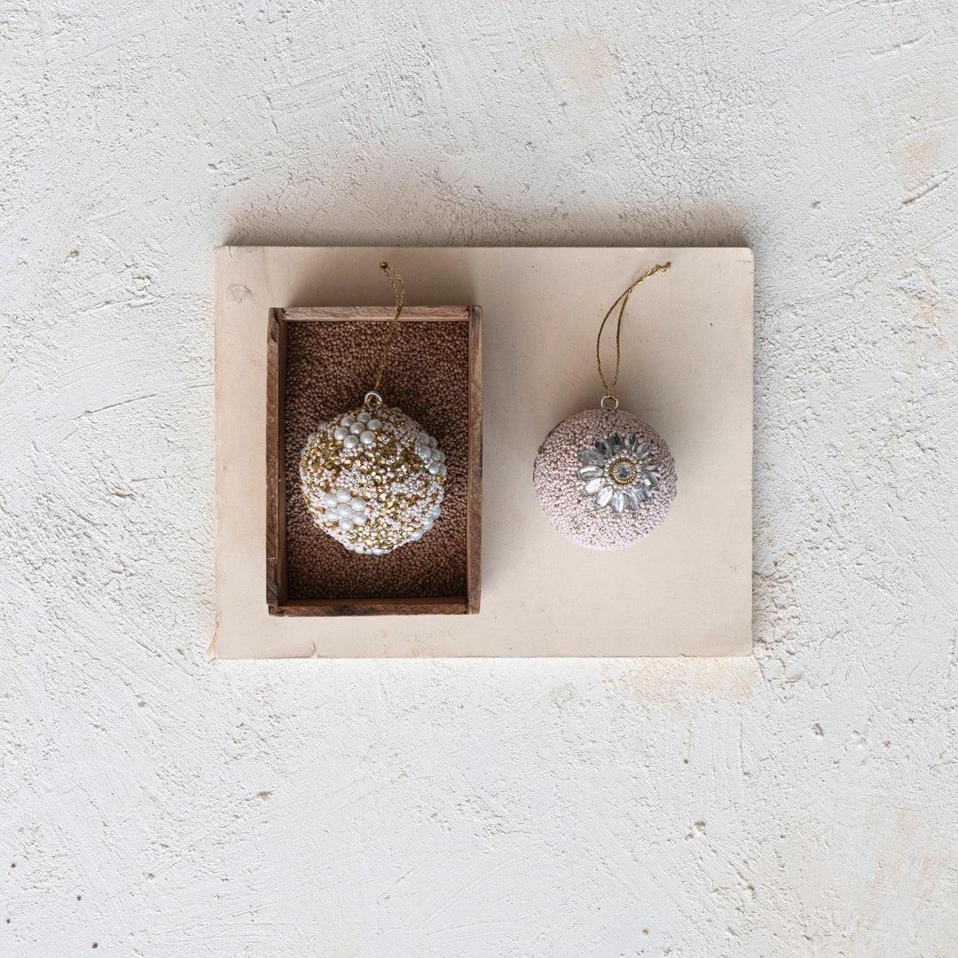 Two round ornaments with beads, sequins, and jewels: one with gold glitter and pearls, one with pink sequins and a central embellishment.