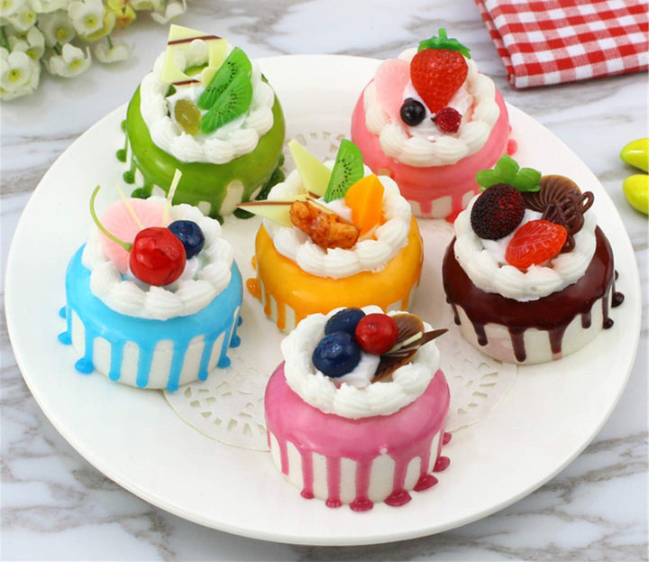 Six colorful faux mini cakes with frosting and fruit accents, available in various sizes.