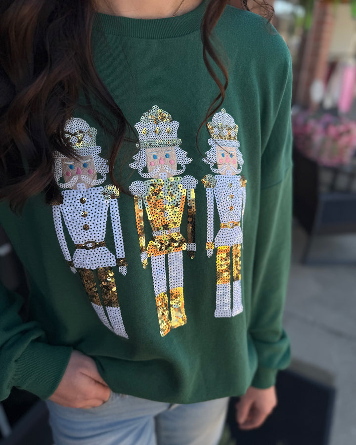 Dark green Alpine Nutcracker sequin sweatshirt featuring three gold and silver sequined nutcracker soldiers. Available in various sizes.