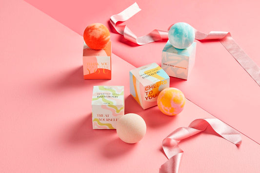 Four colorful scented bath bombs with decorative gift boxes and uplifting messages. Sizes unavailable.