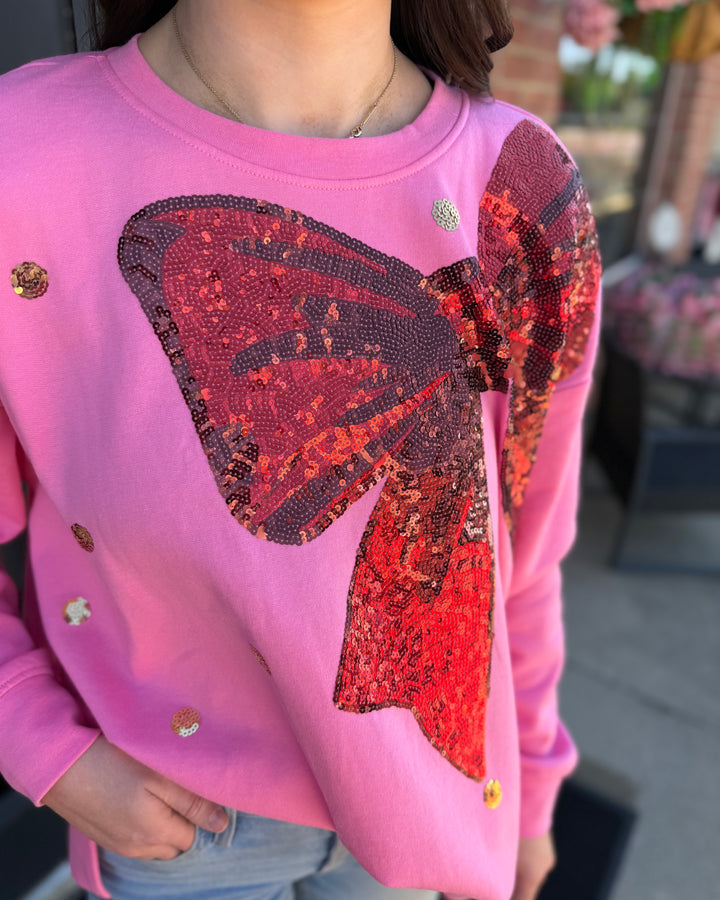 Relaxed pink sweatshirt with a large red sequin bow and gold sequin accents.