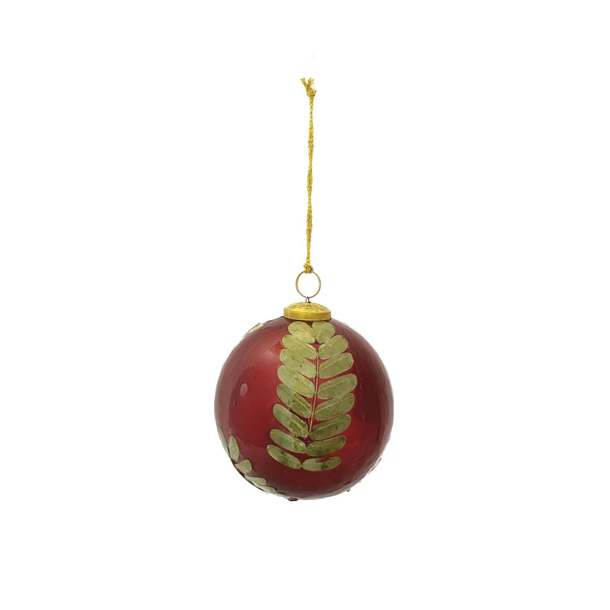 Red glass ball ornament with embedded gold-toned eucalyptus leaves and gold hanging string.