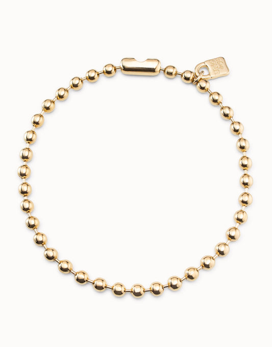 Short beaded necklace with evenly spaced round gold beads, rectangular padlock clasp, and small tag near clasp, handmade in Spain. Sizes available: short.