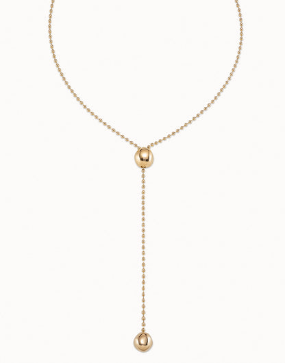 Long Adjustable Chain Necklace, handcrafted in Spain and plated in 18k gold. Features a beaded chain with a central bead, drop chain ending with a larger bead accent, and an adjustable clasp. Available in multiple sizes.