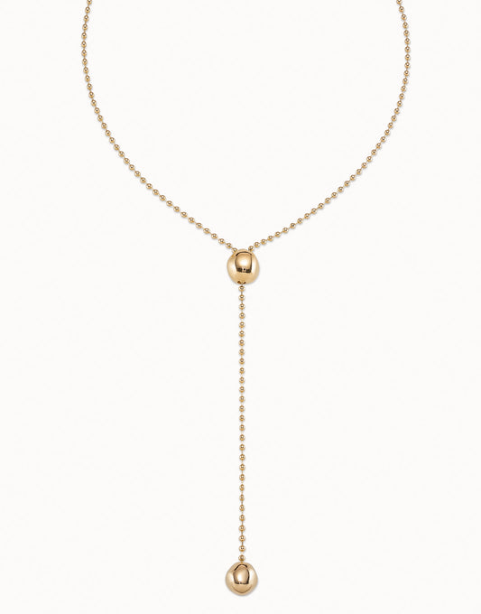 Long Adjustable Chain Necklace, handcrafted in Spain and plated in 18k gold. Features a beaded chain with a central bead, drop chain ending with a larger bead accent, and an adjustable clasp. Available in multiple sizes.