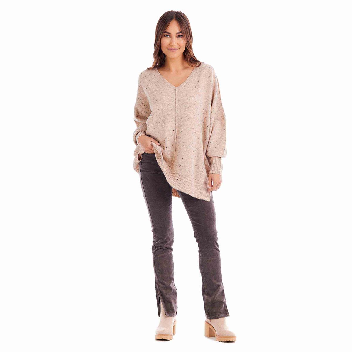 A woman stands confidently in a Cindy V-Neck Sweater, crafted from luxurious speckled fuzzy yarn. Complemented with dark gray jeans and beige high heels, she has a subtle smile and