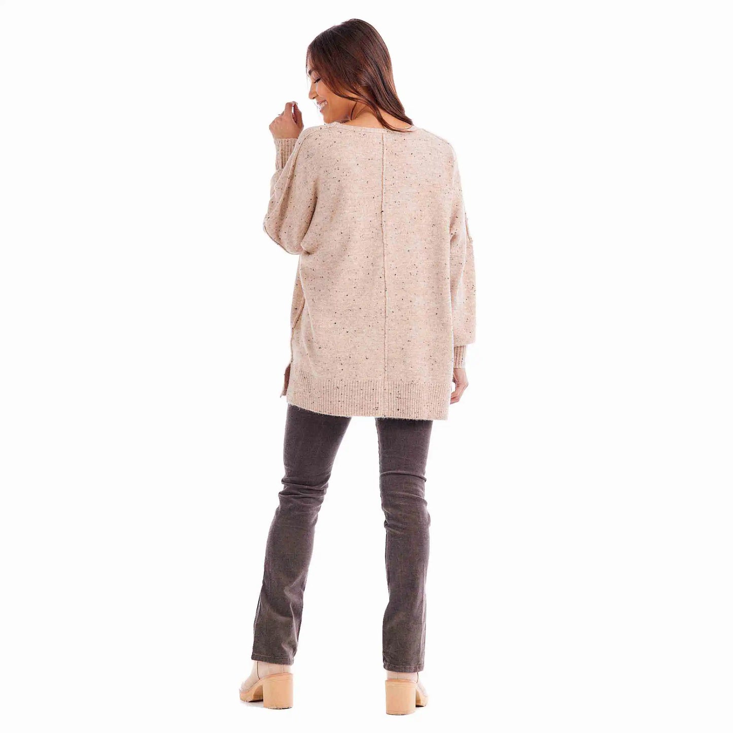 A woman standing with her back to the camera, wearing a Lululemon V-Neck Sweater in beige, gray jeans, and beige high heels, isolated on a white background.