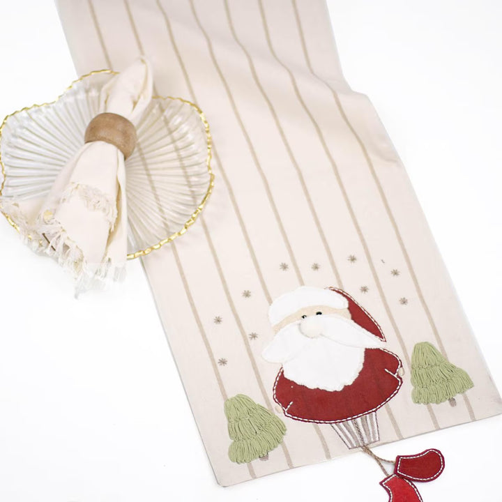 Old St. Nick Christmas Table Runner in cream with thin vertical stripes, featuring a Santa in a hot air balloon appliqué and two embroidered trees.