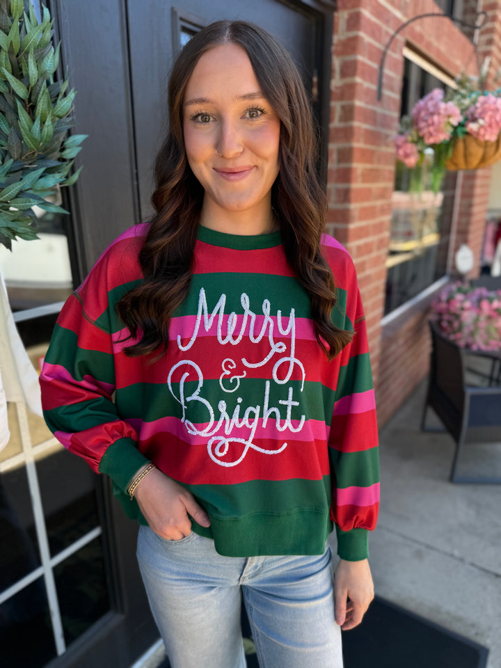 Millie Merry &amp; Bright red and green striped sweatshirt with white glittery “Merry &amp; Bright” text.