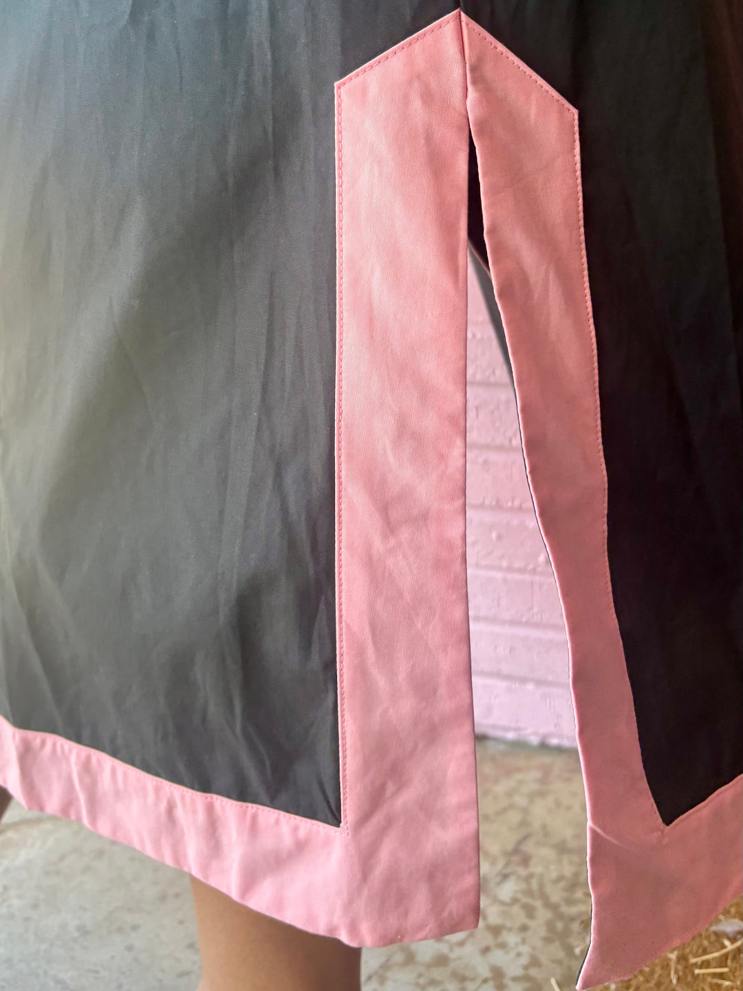 Bottom corner of the Black Floral Appliqué Midi Dress with pink trim and side slit. Available in sizes XS–XL.