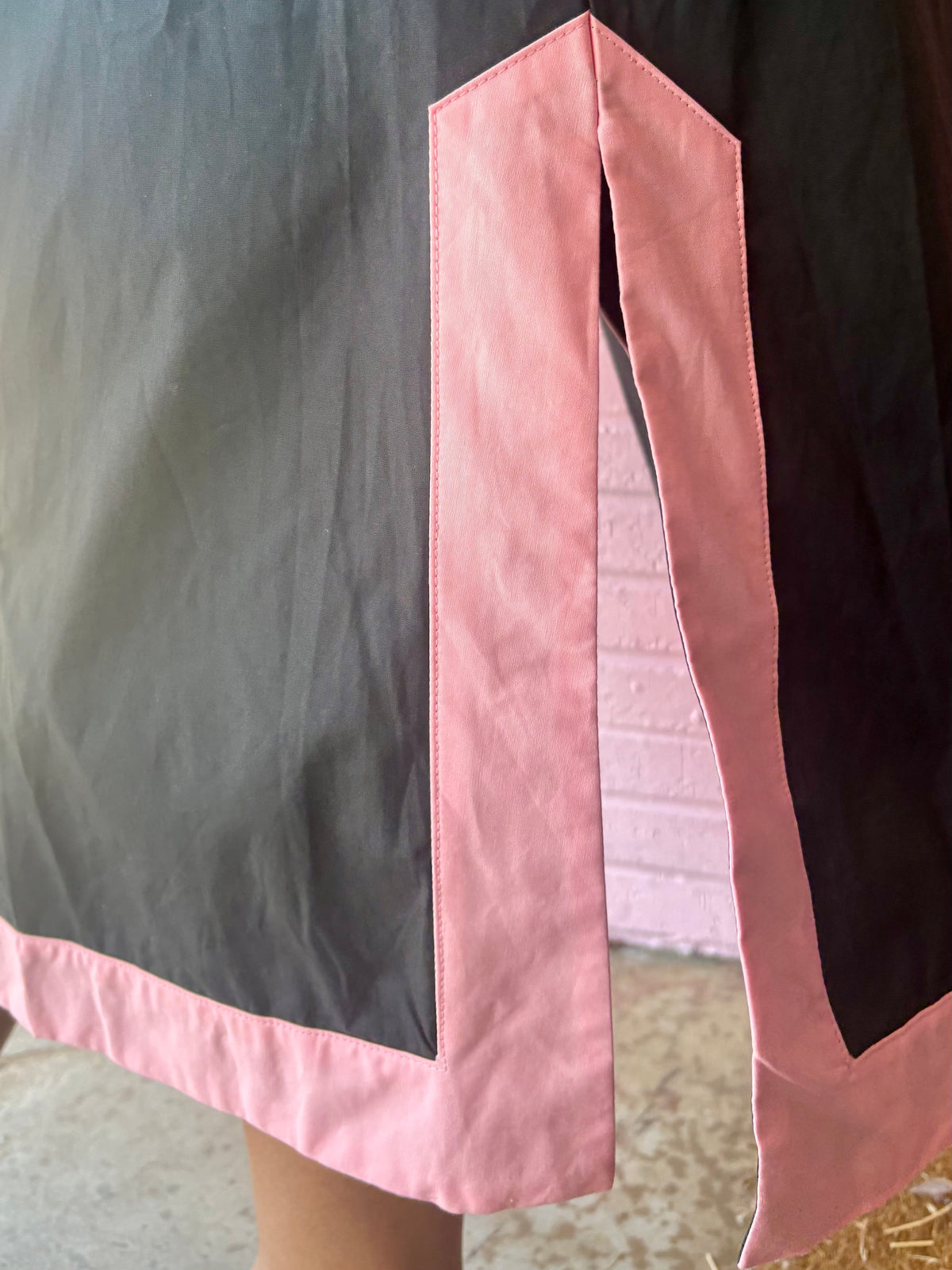 Bottom corner of the Black Floral Appliqué Midi Dress with pink trim and side slit. Available in sizes XS–XL.