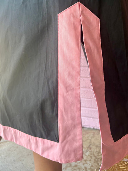 Bottom corner of the Black Floral Appliqué Midi Dress with pink trim and side slit. Available in sizes XS–XL.