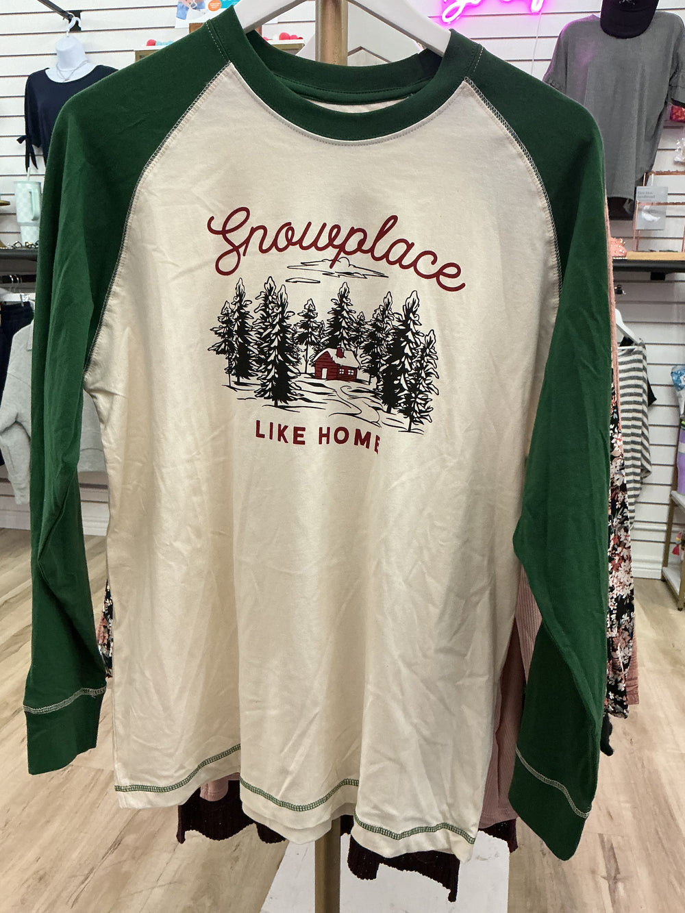 Men’s Snow Place Like Home Baseball T-Shirt, cream tee with green sleeves and a “Snowplace LIKE HOME” forest cabin graphic.
