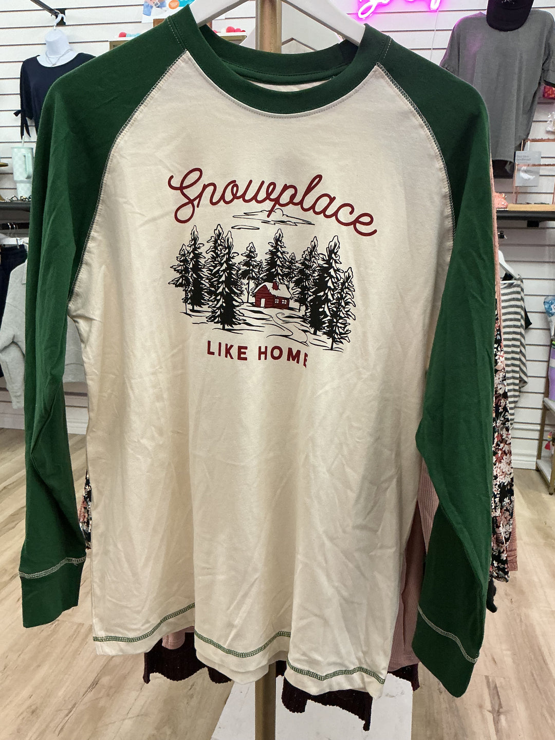 Men’s Snow Place Like Home Baseball T-Shirt, cream tee with green sleeves and a “Snowplace LIKE HOME” forest cabin graphic.