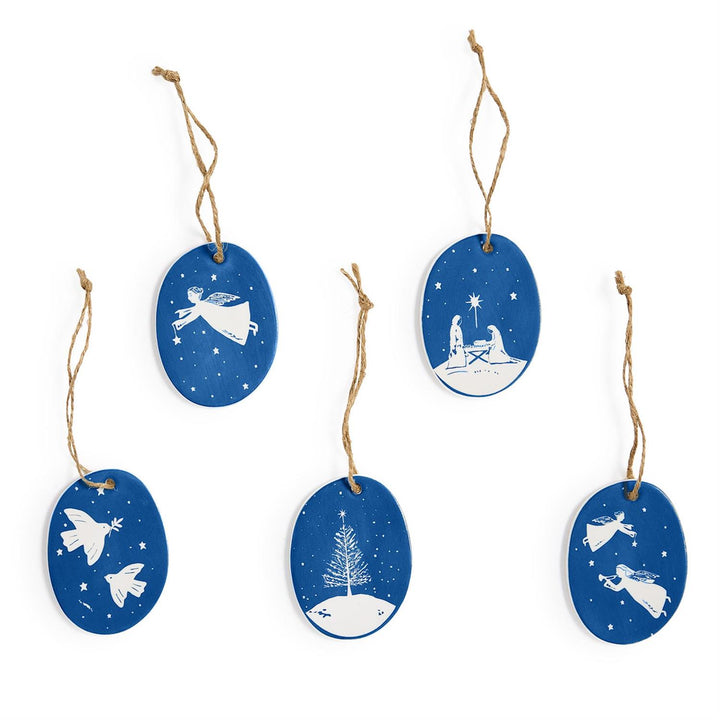 Five oval blue and white porcelain ornaments featuring angels, doves, a nativity, and a pine tree, with twine loops.