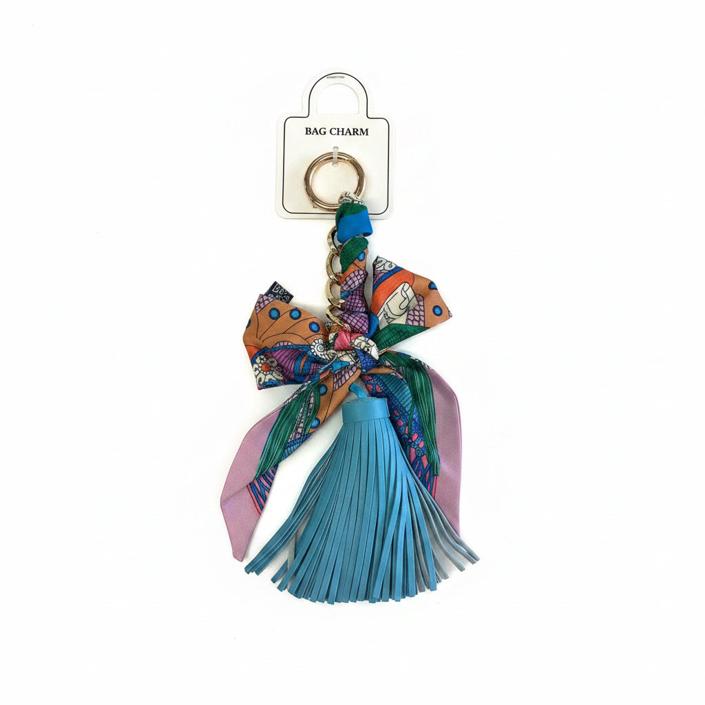 Blue faux leather tassel bag charm with vibrant patterned bow, gold keyring, and square “BAG CHARM” tag. Sizes available: small, medium, large.